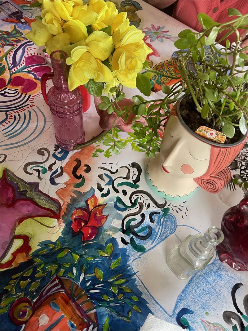 Colourful drawing materials and flowers spread across the workshop table