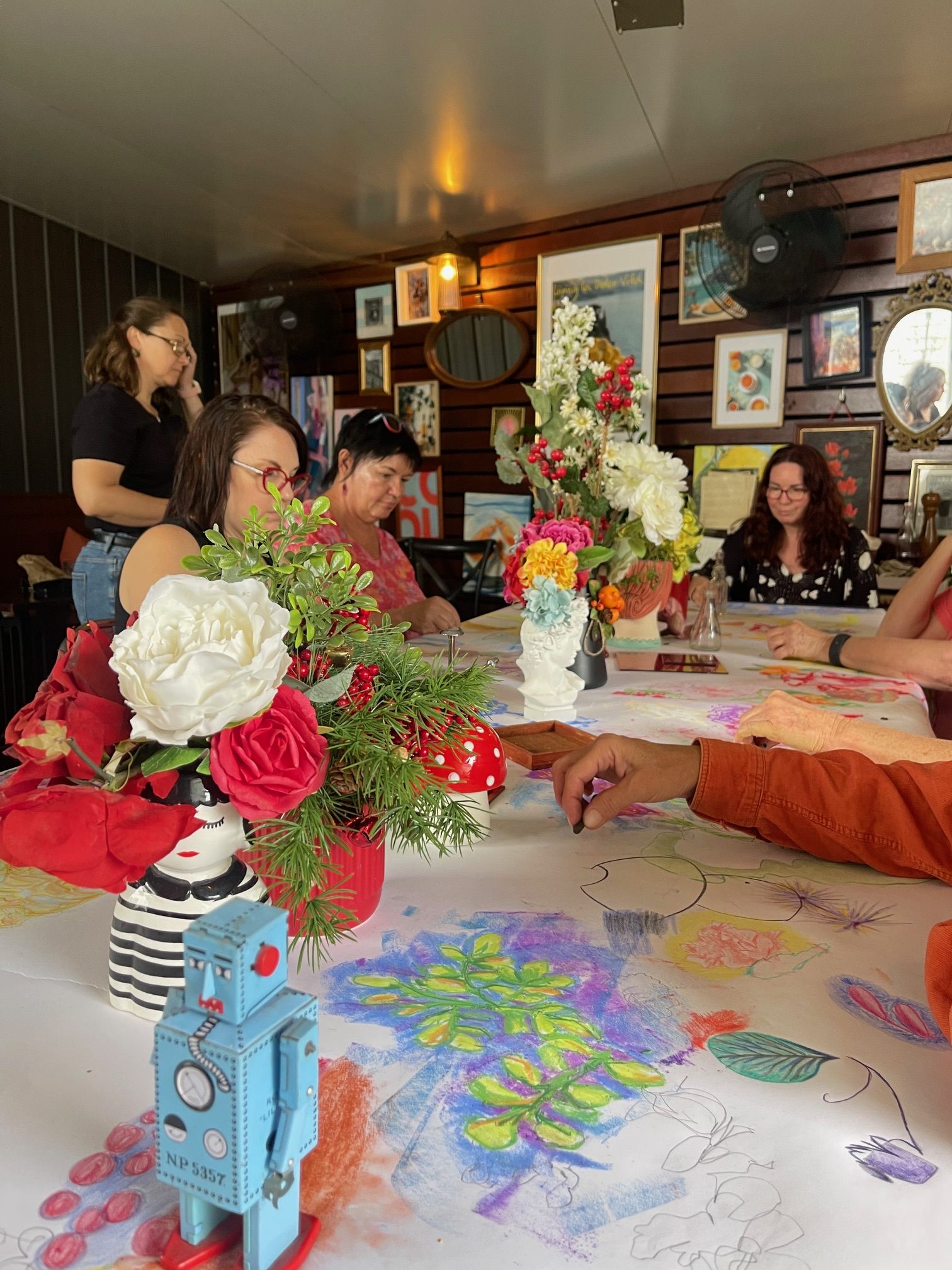 Workshop participants sketching around a flower-filled table with a blue robot centerpiece